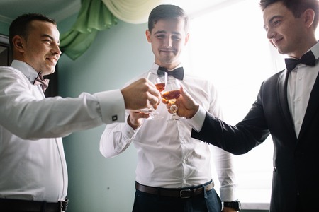 stylish groomsmen helping happy groom getting ready in the morningの写真素材