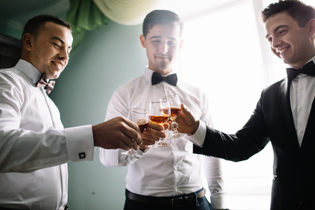 stylish groomsmen helping happy groom getting ready in the morningの写真素材