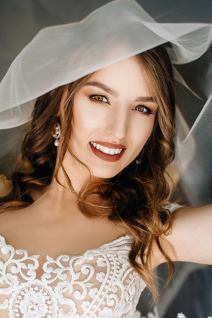 Beautiful sexy bride in white dress posing under curtainの写真素材