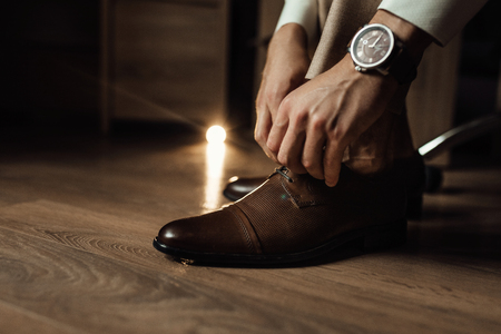 The groom is gathering in the morning. A gray chair. Men's Black classic patent leather shoes. Wedding details. The groom ties up the shoelaces.の写真素材
