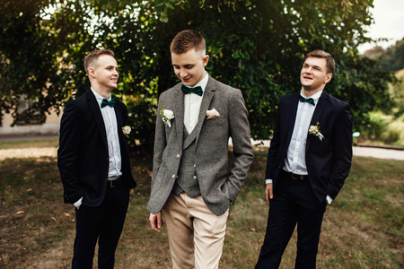 Laughing groomsmen in suits hold smiling groom under his armsの写真素材