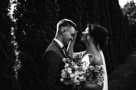 Beautiful happy young bride walking with with handsome groom in sunlit parkの写真素材
