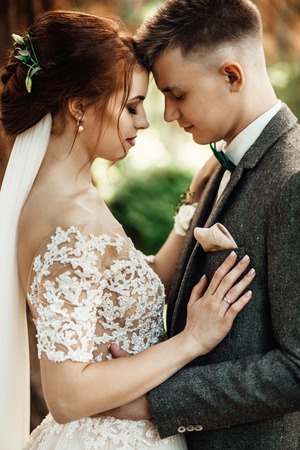 Sun illuminates tender faces of pretty wedding couple huggingの写真素材