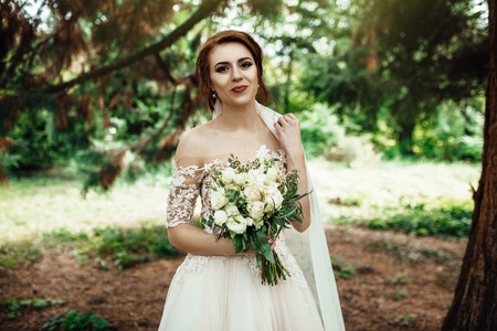 Stunning bride in elegant dress poses in the green parkの写真素材