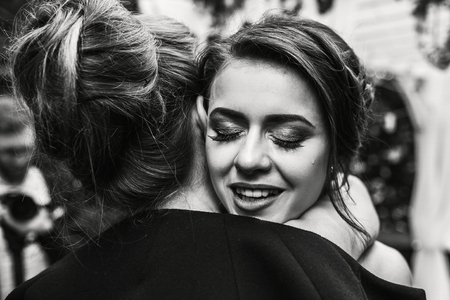 Bride in lace dress hugs woman in peeach gown tenderの写真素材