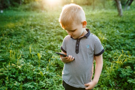 Little cute boy holding phone in his hand and smiles in summer gの写真素材