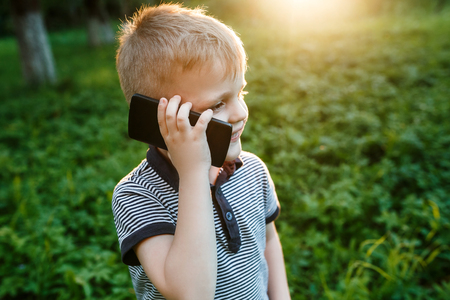 Little cute boy holding phone in his hand and smiles in summer gの写真素材