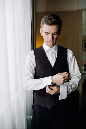 stylish groom portrait at the window while getting ready in theの写真素材