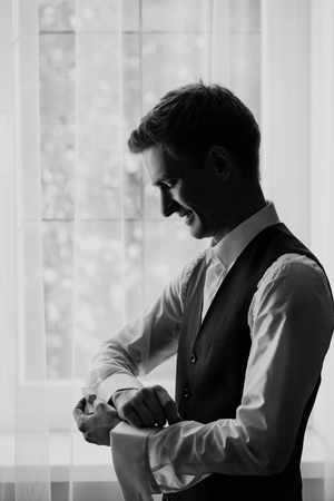 stylish groom portrait at the window while getting ready in theの写真素材
