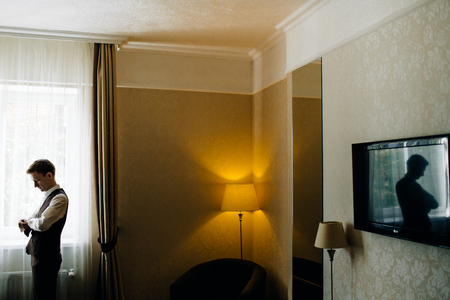 stylish groom portrait at the window while getting ready in theの写真素材