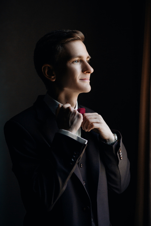 stylish groom portrait at the window while getting ready in theの写真素材