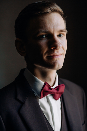 stylish groom portrait at the window while getting ready in theの写真素材