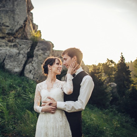 Romantic newlywed couple posing in sunset lights on majestic rocの写真素材