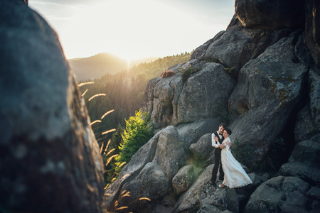Romantic newlywed couple posing in sunset lights on majestic rocの写真素材