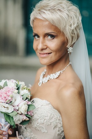 Smiling bride stands with a white bouquet in a green gardenの写真素材