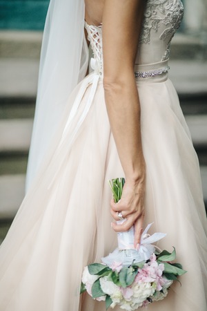 Stunning bride with red bouquet stands on the streetの写真素材