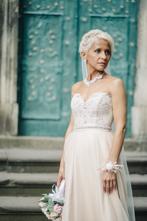 Smiling bride stands with a white bouquet in a green gardenの写真素材