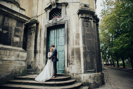 Elegant bride with groom walking near old catholic cathedralの写真素材