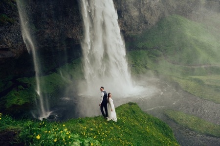 Bride and groom walking in Iceland. Icelandic waterfall on the bの写真素材