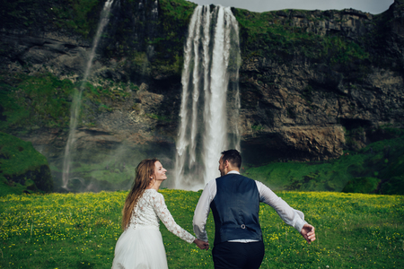 Bride and groom walking in Iceland. Icelandic waterfall on the bの写真素材