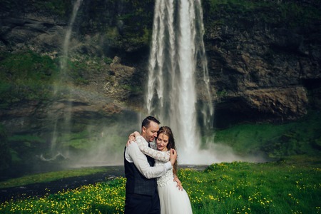 Bride and groom walking in Iceland. Icelandic waterfall on the bの写真素材