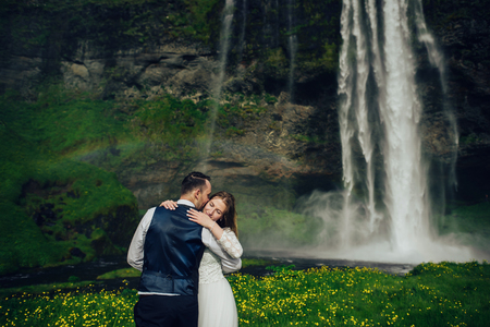 Bride and groom walking in Iceland. Icelandic waterfall on the bの写真素材