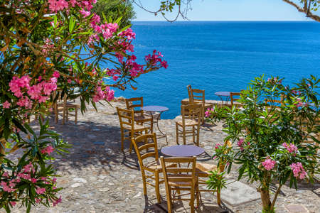 Traditional cafe exterior in the fortified medieval  castle of Monemvasia. Iron tables, wooden chairs and   flowers   with the view of the  aegean sea in the background.の写真素材