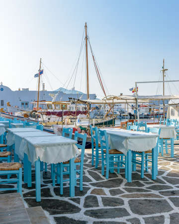 Moored traditional fishing boats and the exterior of a fish tavern with  tables and wooden chairs on the picturesque harbor of Naousa Paros, Greece.の写真素材