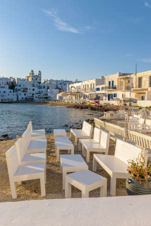 Traditional Cycladitic view with an exterior of a bar besides the sea and  whitewashed houses with the christian church of kimisis Theotokou during afternoon in Naousa  Paros island, Greeceの写真素材