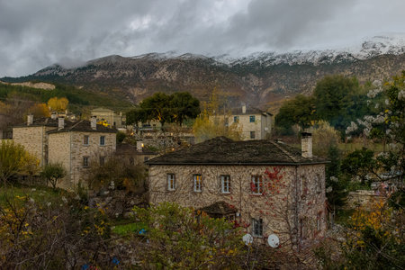 Î¤raditional architecture  with the stone buildings and snowy mountains as background during  fall season in the picturesque village of papigo , zagori Greeceの写真素材