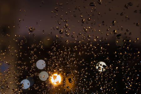 drops after rain on the glass of a home window in the late evening with a blurred background and bright lightsの写真素材
