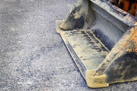 the empty dirty bucket of a small tractor lies on the pavement. The concept of repair, house...