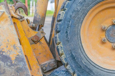 Scratched metal bucket of a small old orange tractor. old tractor wheel. road construction, repair...