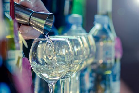 the bartenderâ€™s hand with the help of a dispenser pours an alcoholic drink into a glass with...