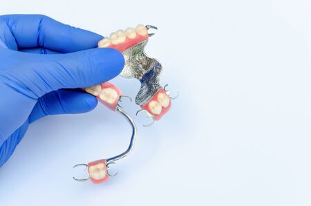 orthopedic dentistry. prosthetics concept with removable dentures. a dentistâs hand in a glove holds a set of clasp prostheses on the upper and lower jaws. light backgroundの写真素材