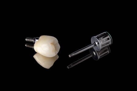 ceramic tooth on the implant with pronounced anatomy and a metal screwdriver for twisting the crown to the implant. isolated on a black background. orthopedic dentistry. dental implantation conceptの写真素材