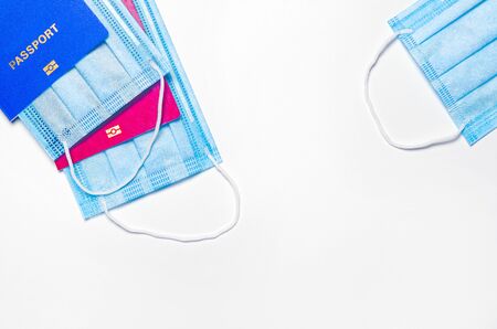 foreign passports of red and blue colors with medical face masks in the left corner and a medical mask in the right corner on a light background. travel during quarantine. closed borders concept. copy space. flat layの写真素材
