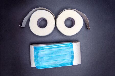 toilet paper rolls are laid out in the form of an emoticon with a blue medical face mask. on a black background. virus outbreak concept. coronavirus newsの写真素材