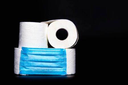 rolls of white toilet paper with a blue medical face mask are on a black background. coronavirus outbreak panic conceptの写真素材