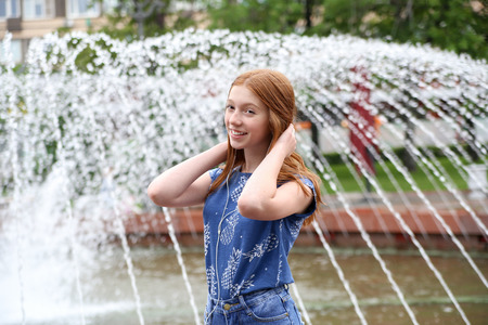 A young girl listens to music in your phone near the fountain in the cityの写真素材