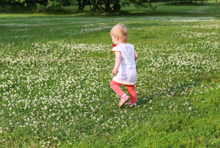 Little girl runs across a large field dotted with clover.の写真素材