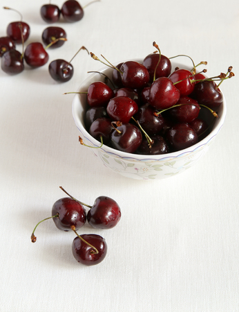 Fresh cherries in bowl and kitchen napkin.  White cloth from flax. Healthy food concept.の写真素材