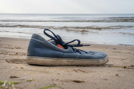 Lonely tossed blue, male sports shoes by the sea.in the sand forgotten standing blue sports shoesの写真素材