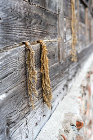 Background image. Pieces of linen tow rope protrude from a gap in an old wooden wall, where this material is used as a gap closureの写真素材