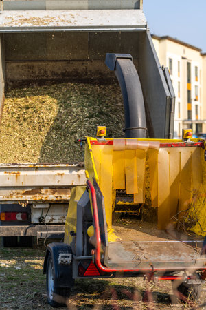 On a sunny spring working day, the arborist's dump truck, together with a branch chipper, is located in a filled meadow with residential houses in the background.の写真素材