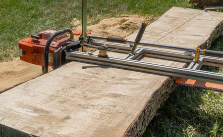 sawing a large log tree lying on the ground using a chainsaw millの写真素材