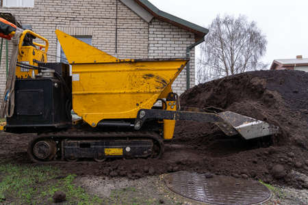 The small tractor tracked dumpster moves the fertile soil, helping the gardener to set up the...