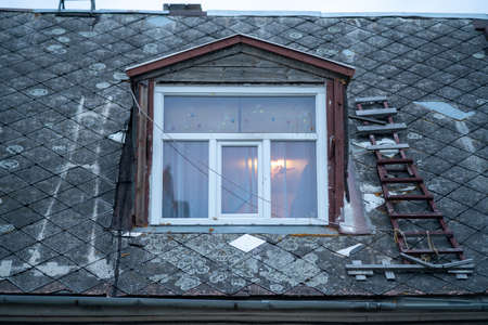 an old building with a slate roof and a floor-standing window with a wooden staircase on one side of the roof, and only a footprint of the stairs can be seen on the roof side on the other side of the windowの写真素材