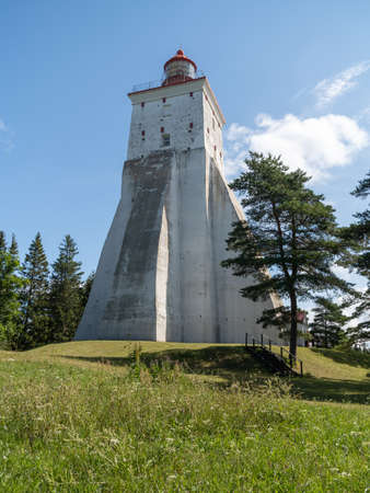 Estonia, Hiiumaa Island. View of the old massive masonry lighthouse statically rises above the tops of the treesSummer sunlit white, masonry lighthouse at the top of a hill against a bluish sky backgroundの写真素材