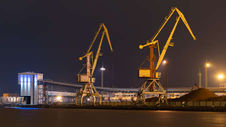 On the other side of the Venta canal you can see the harbor with two yellow harbor cranes, buildings and peat piles.の写真素材